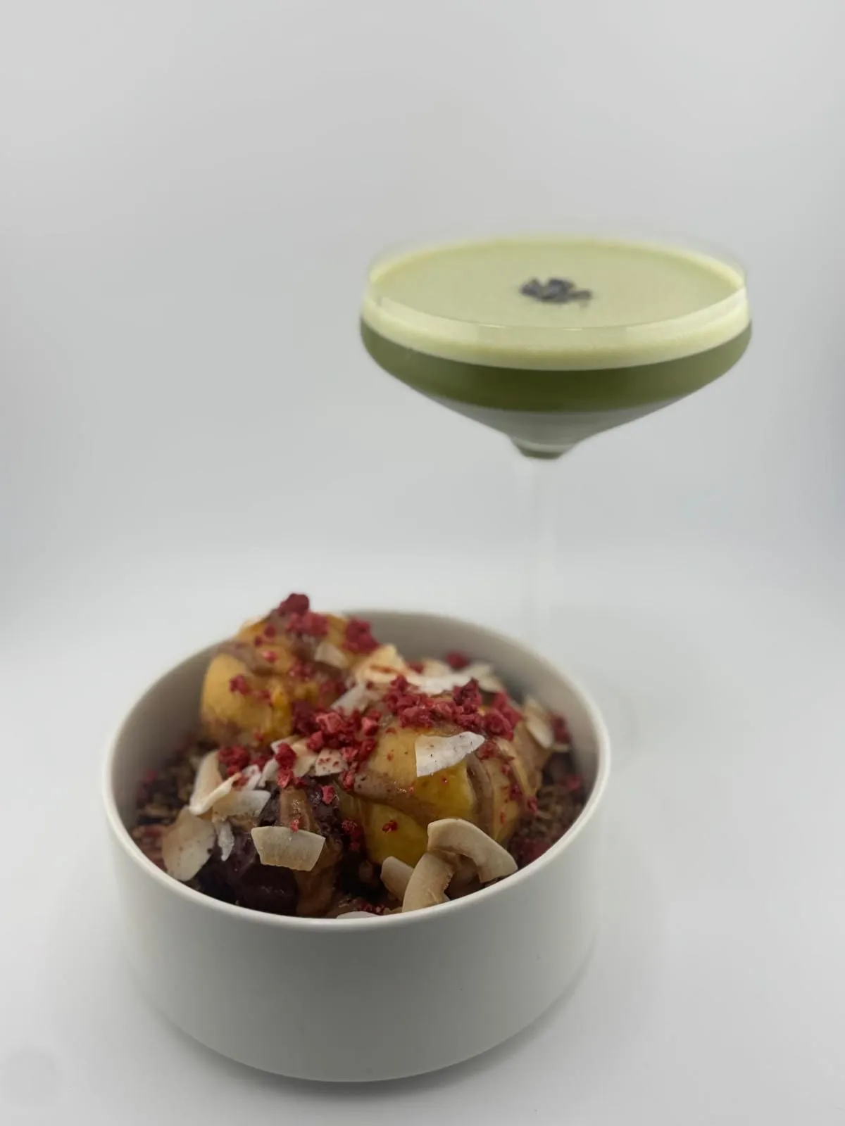 Açaí-Mango-Bowl mit Himbeeren und Kokoschips, daneben ein grüner Matcha Martini