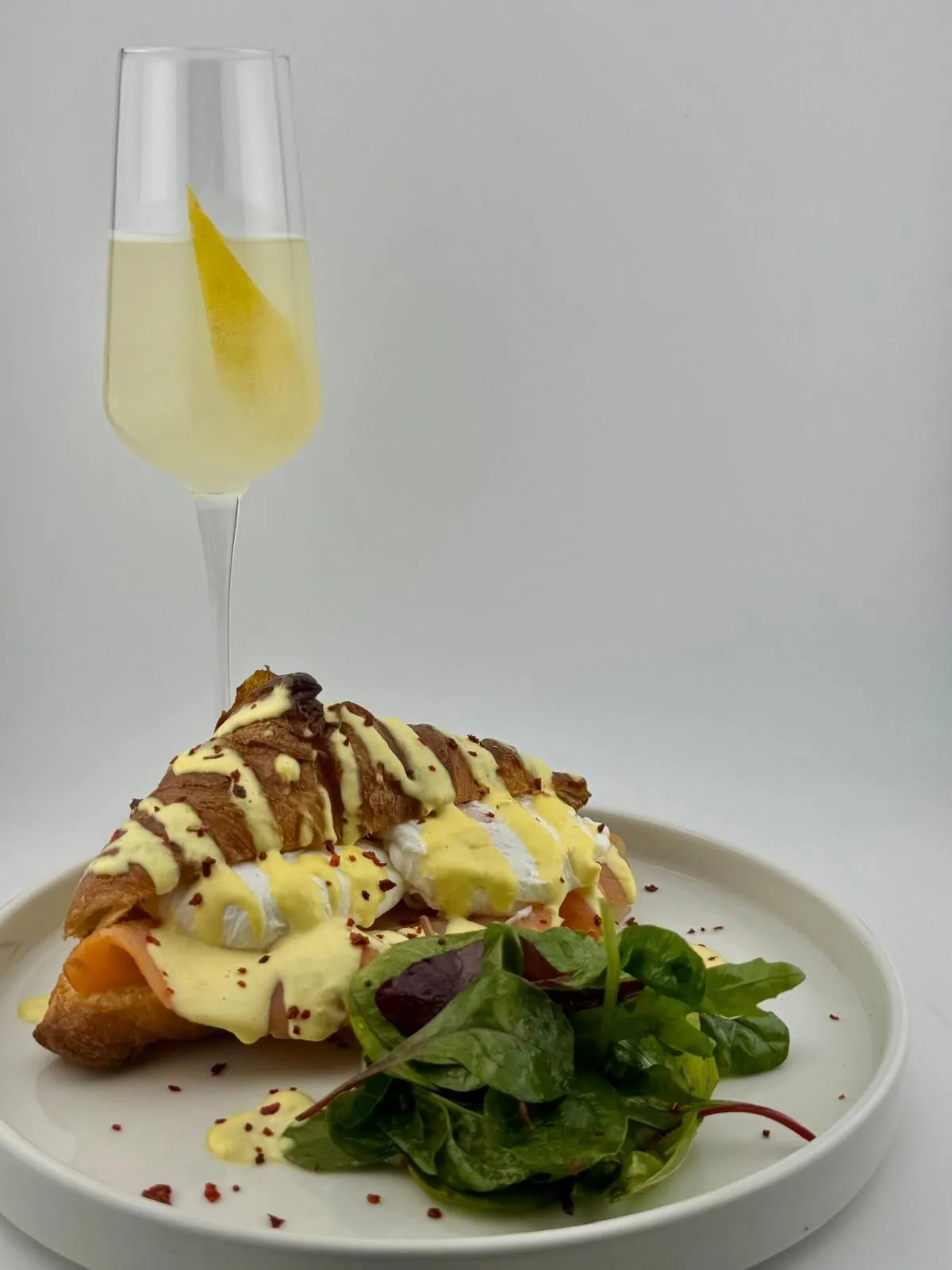 Eggs Benedict mit Lachs im Croissant, Sauce Hollandaise, daneben ein French 75 im Sektglas