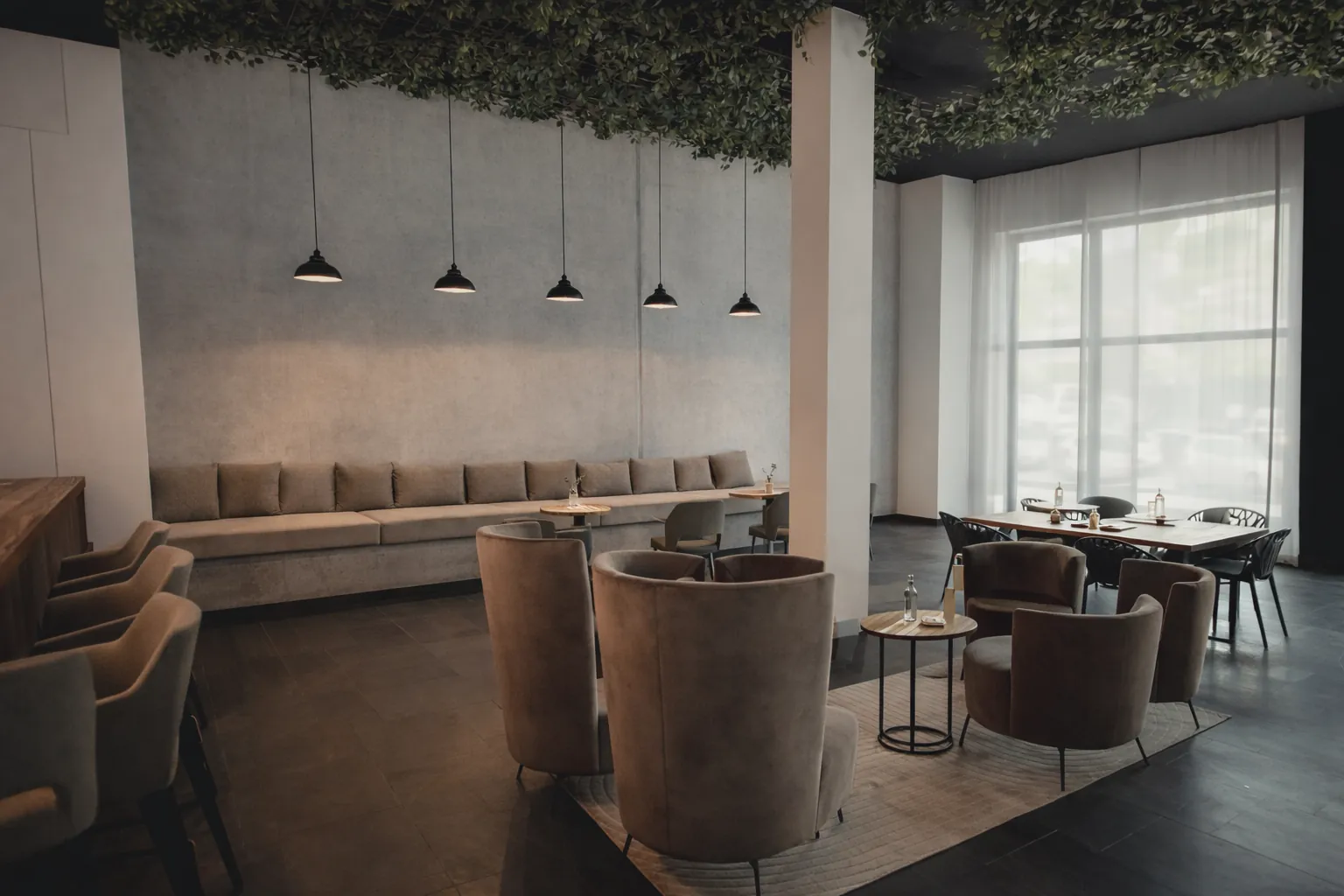 Der Gastraum als Event-Setting: Sessel, Sofas und Tische unter Pendelleuchten und Pflanzendecke
